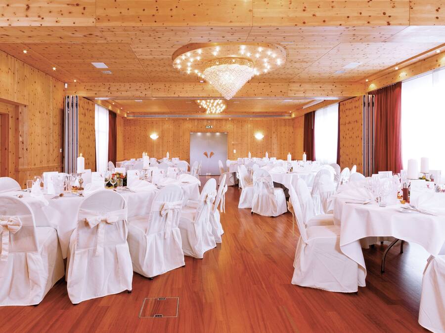 Ein großer Festsaal mit Holzwänden und -decke, weißen Tischdecken und Stühlen.
