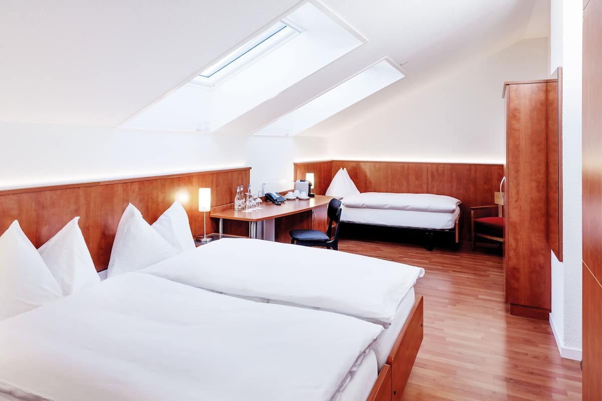 Habitación de hotel con dos camas, un escritorio y una silla. Hay un tragaluz sobre el escritorio y un armario a la derecha.