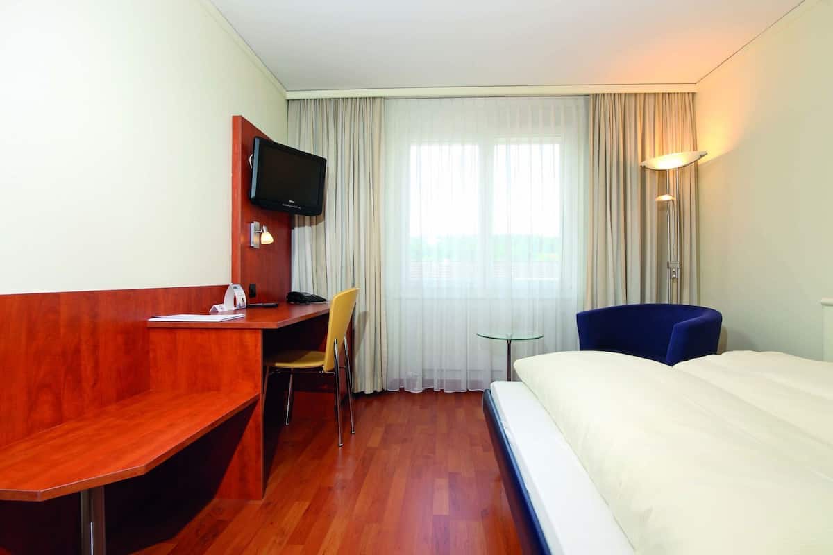 Una habitación de hotel con cama, escritorio, silla, televisor y lámpara.