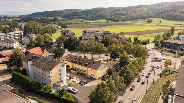 Un hôtel à plusieurs étages doté d’un parking et offrant une vue sur un champ verdoyant et des collines en arrière-plan.