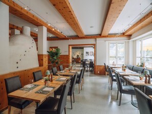 A restaurant with wooden beams, tables with chairs, and a large white chimney.