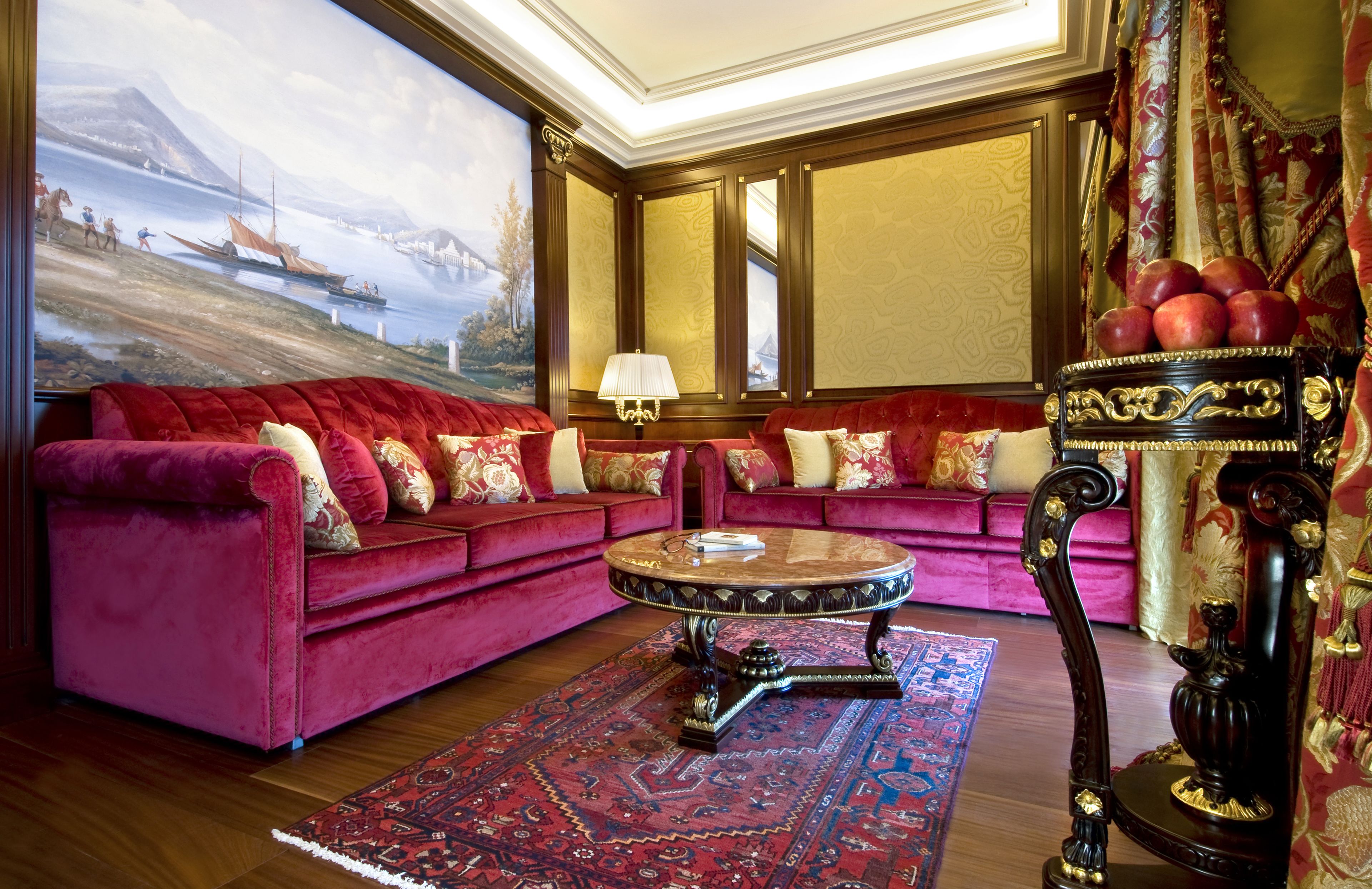 Una habitación lujosa con un sofá de terciopelo rojo, una mesita de centro redonda y una mesita auxiliar decorada con manzanas.