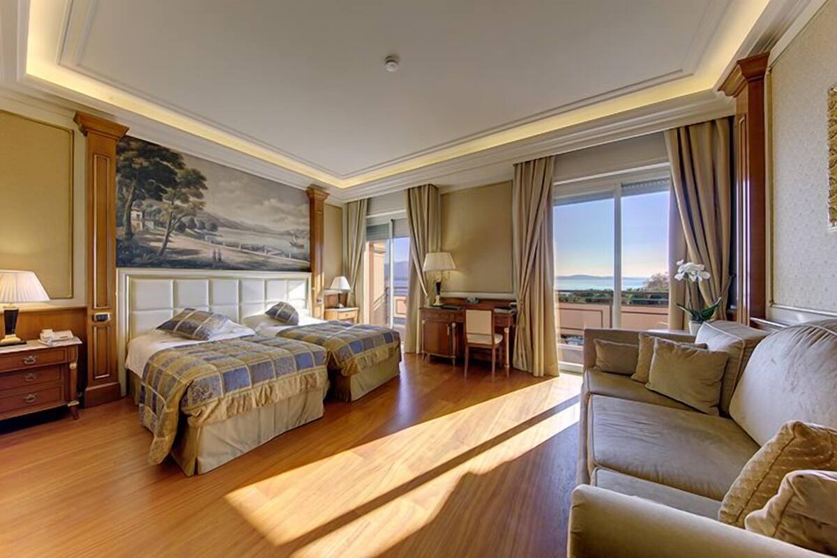 A hotel room with two beds, a sofa, a desk, and a large window with a view.