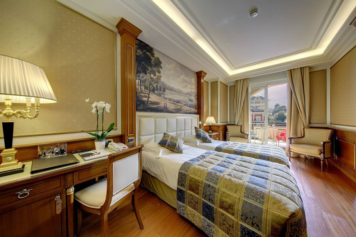 A hotel room with a large bed, a desk with a lamp, a chair, and a view of the outside.