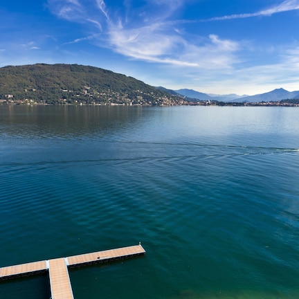 A calm lake with a wooden dock extending into the water, surrounded by mountains and a clear sky.