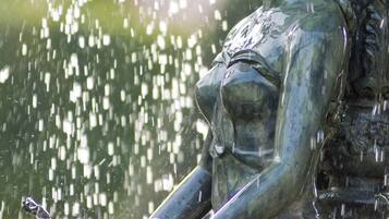 Eine bronzene Statue einer Frau, von deren Händen Wasser herfällt.