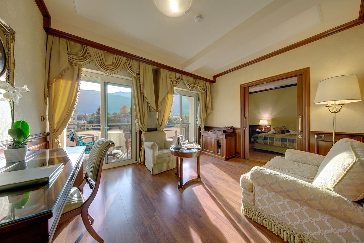 A spacious living area with a dining table, comfortable seating, a view through a large window, and a separate bedroom visible through an open door.