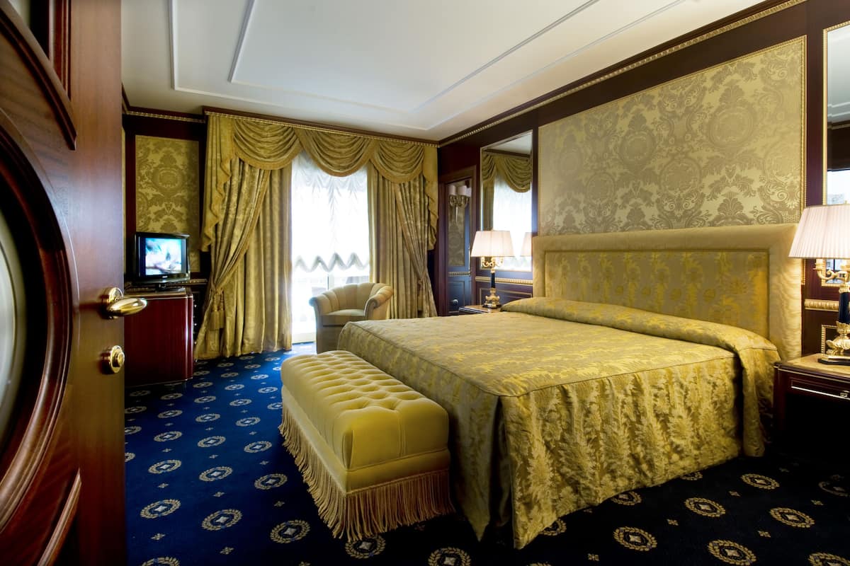 A hotel room with a large bed, a small desk with a television, a chair, and a large mirror.