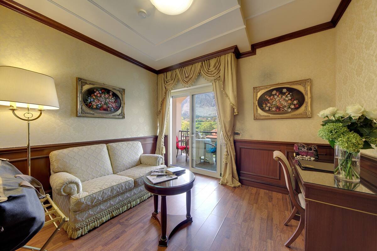 A room with a sofa, a table, a chair, a lamp, and two framed floral paintings.