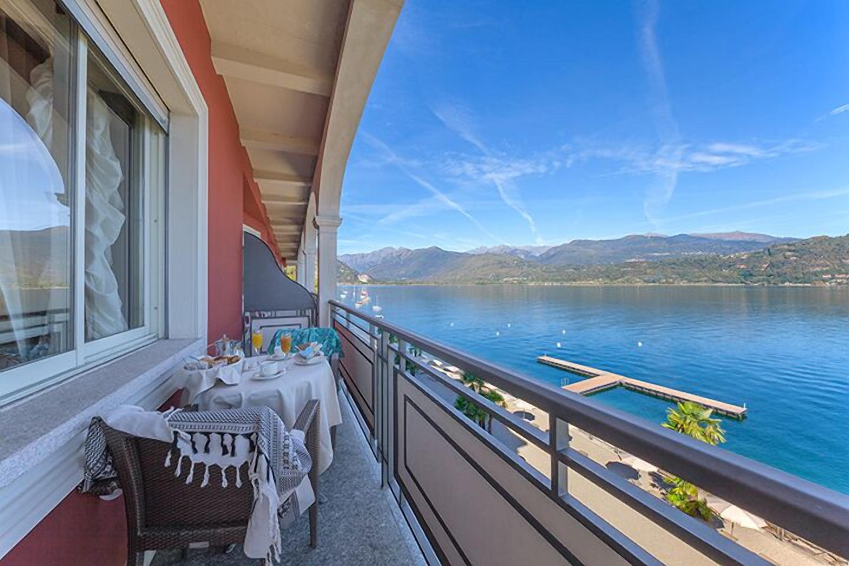 Un balcon avec une table dressée pour le dîner, donnant sur un lac et offrant une vue sur des montagnes en arrière-plan.
