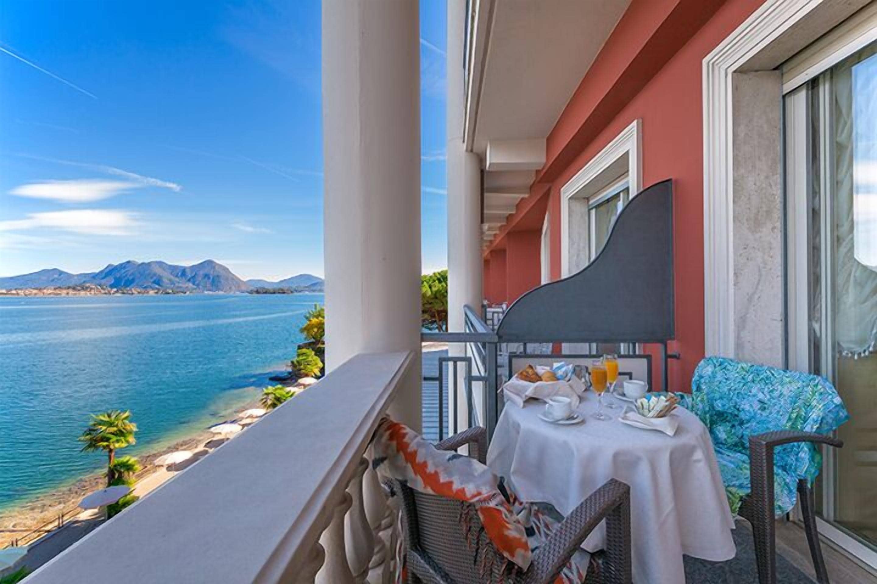 A balcony with a table set for breakfast overlooking a body of water and mountains.