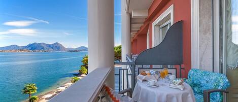 A balcony with a table set for breakfast overlooking a body of water and mountains.