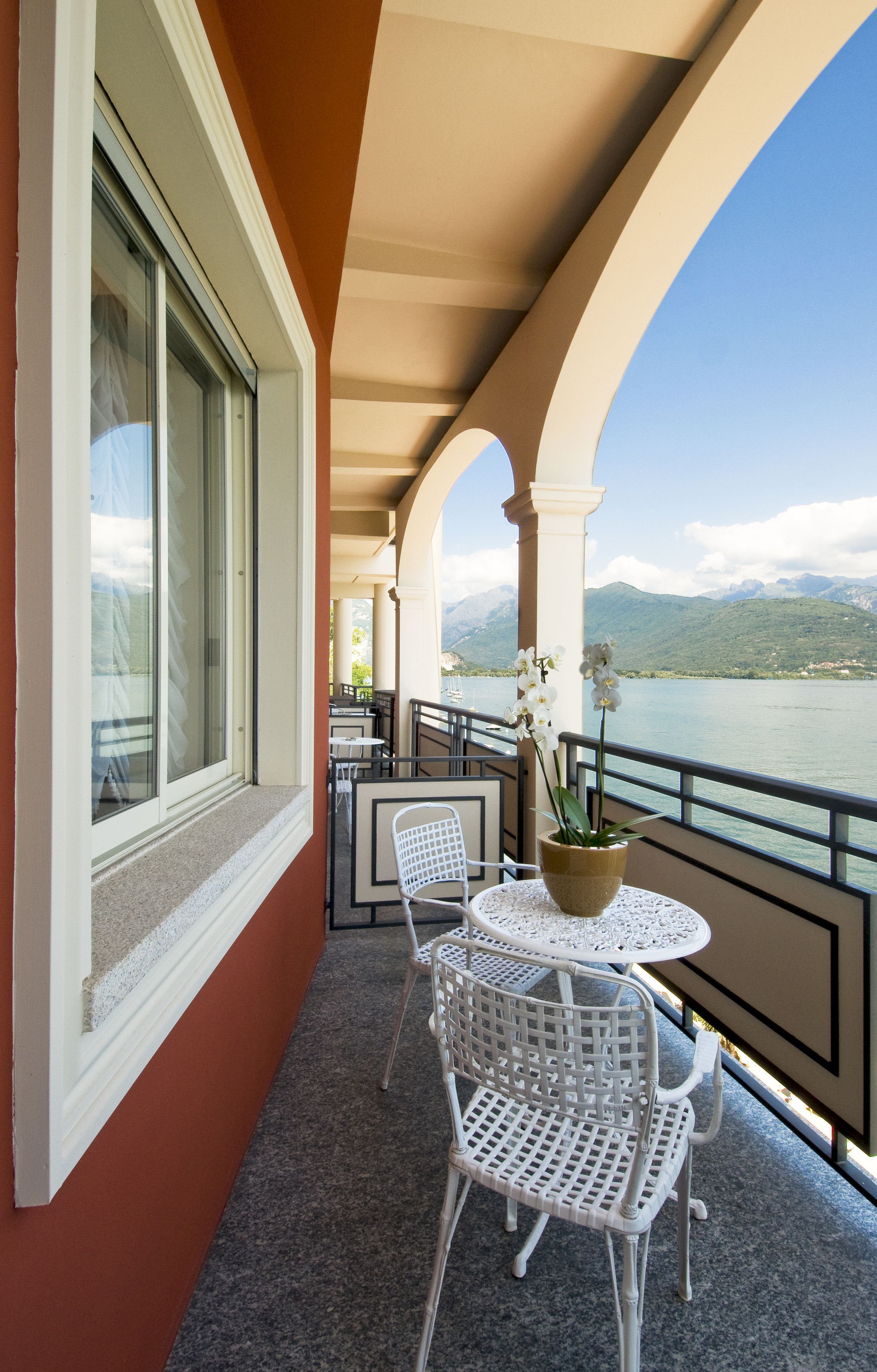 A balcony with a table and chairs, overlooking a lake with mountains in the background.