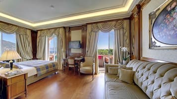 A hotel room with a bed, a sofa, a desk with a chair, a TV, and a large window with curtains.