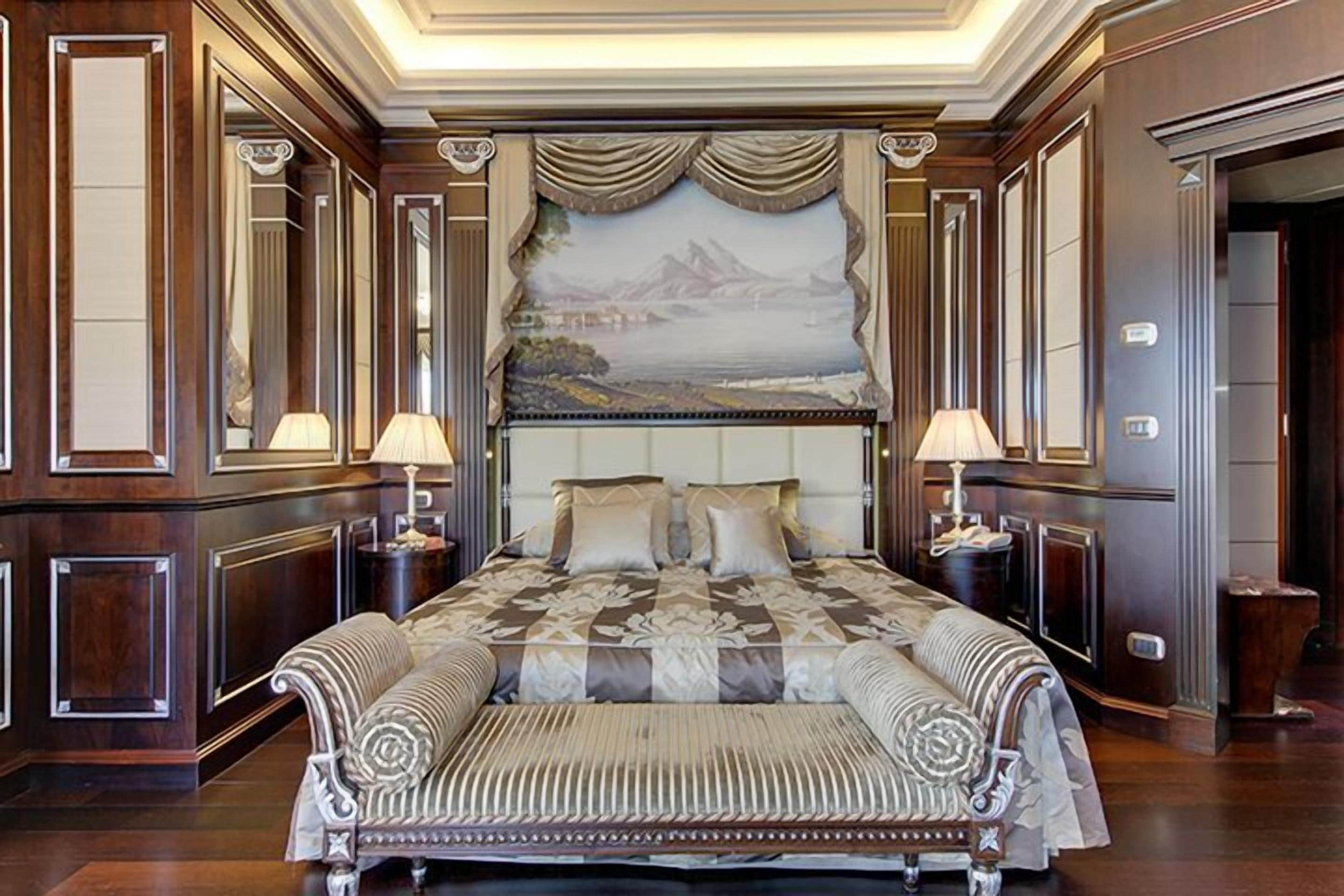 Uma cama grande com cabeceira, duas mesas de cabeceira e um banco ao pé da cama.