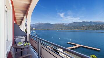 Un balcon agrémenté de meubles en osier, une table avec des pommes, et une vue sur un lac avec des montagnes en arrière-plan.