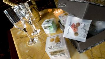 A marble table with two champagne flutes, a box of chocolates, a package of salted peanuts, and a box of hand-made chocolates.