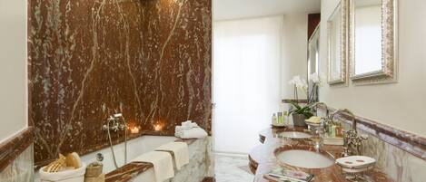 A marble bathroom with a bathtub, two sinks, and a large mirror.