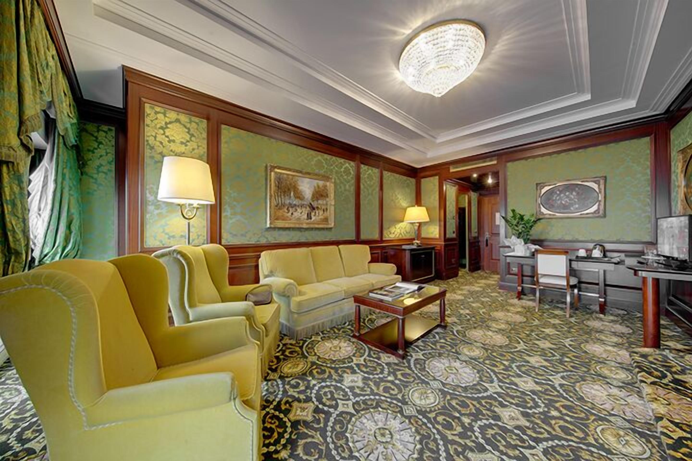 A room with a patterned carpet, a sofa, a coffee table, and a desk with a lamp.