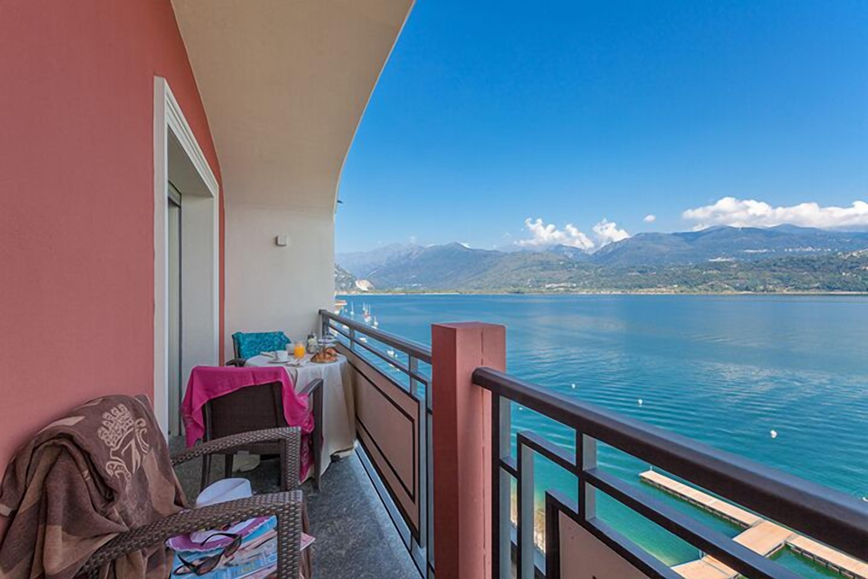 Ein Balkon mit Tisch für zwei Personen, mit Blick auf einen stillen See und Berge im Hintergrund.