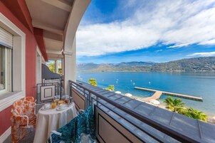Un balcón con mesa lista para el desayuno, con vistas a un lago y montañas al fondo.