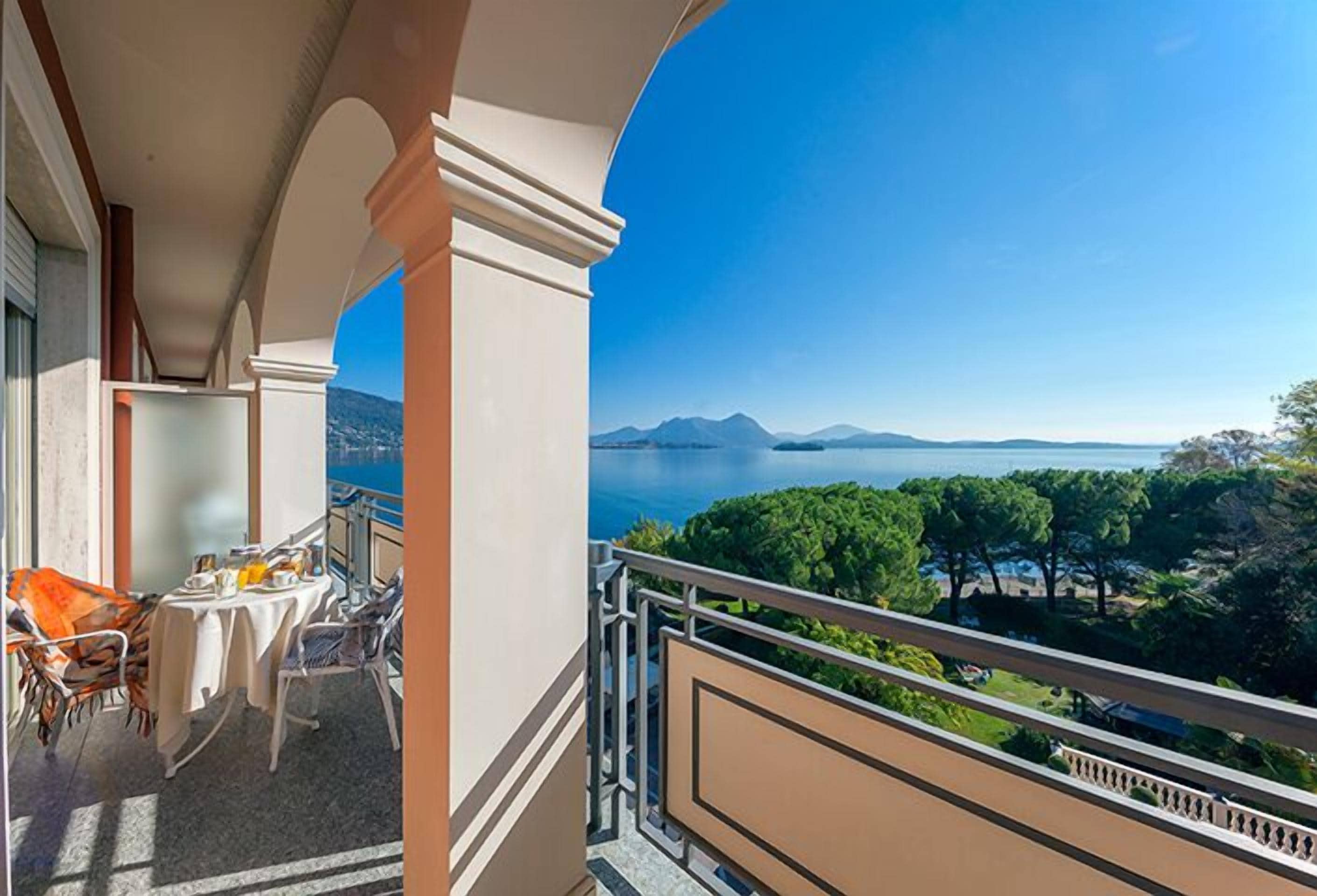 Varanda com uma mesa posta para refeições, oferecendo uma vista panorâmica de um lago e montanhas.