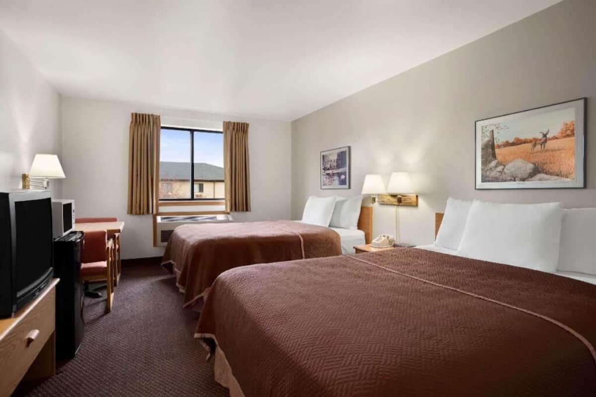 A hotel room with two beds, a desk with a television, and a window with curtains.