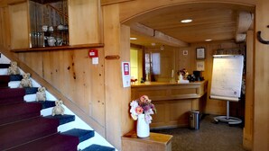 A wooden interior with a staircase, a reception desk, and a whiteboard. - Hotel Bären - The Bear Inn (Wilderswil)