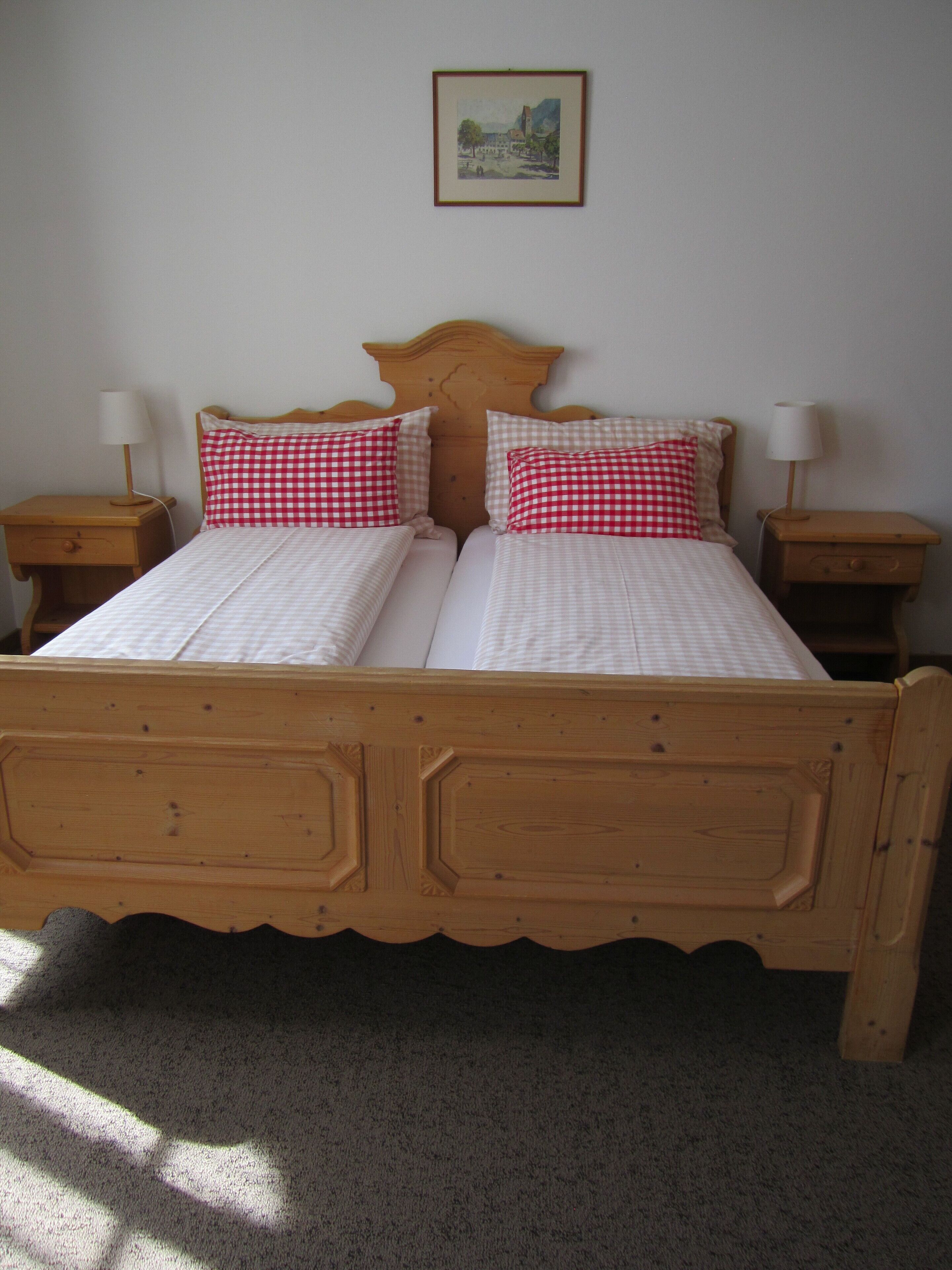 Un lit double avec un cadre en bois, deux tables de chevet et un tableau accroché au mur.