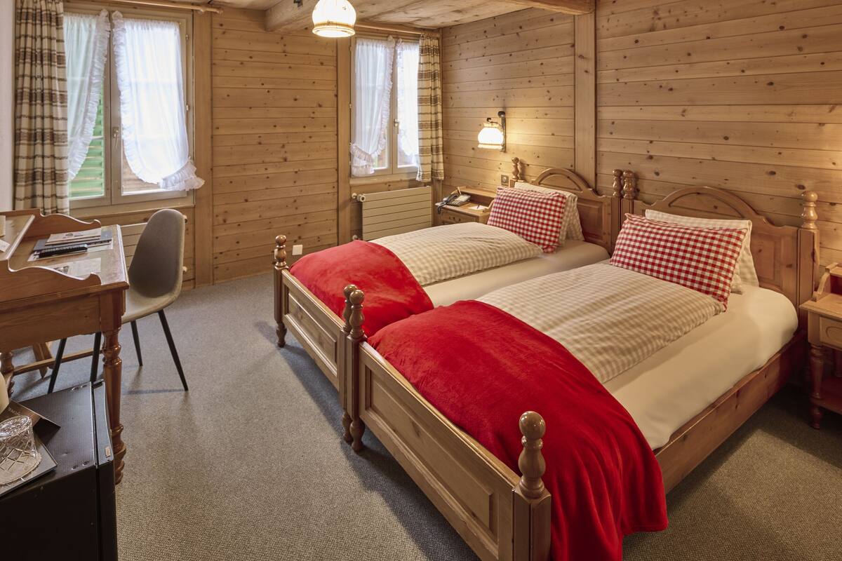 Una habitació amb panells de fusta, amb dos llits, un escriptori amb una cadira i una finestra amb cortines.