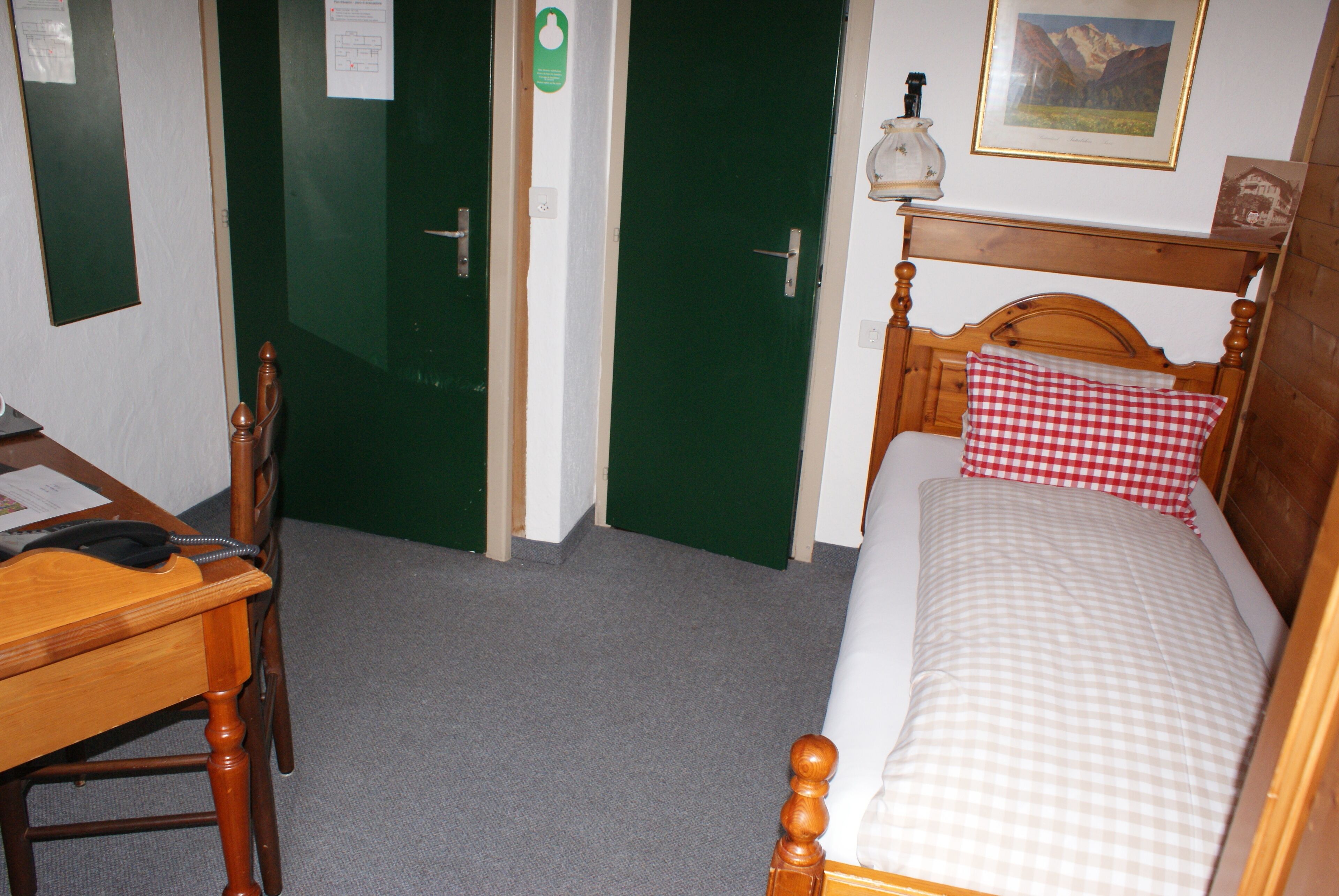 Un dormitorio con una cama de madera, un escritorio y una silla. Hay puertas verdes y un cuadro en la pared.