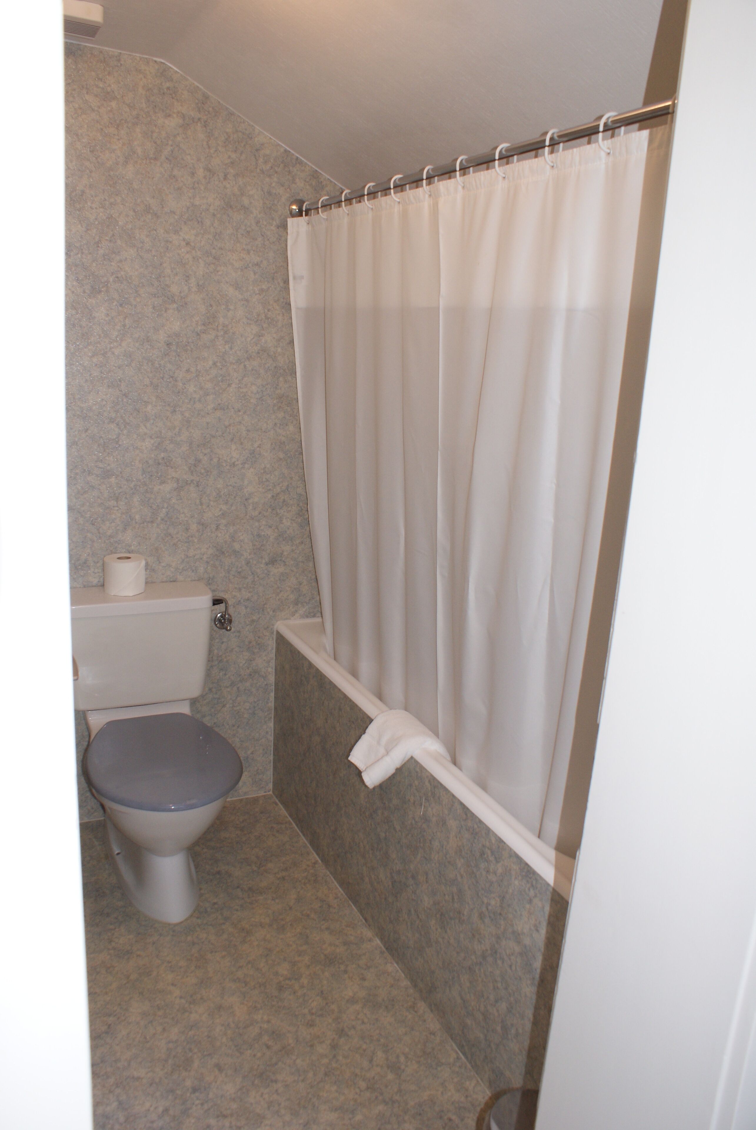 A bathroom with a toilet, a shower curtain, and a bathtub.