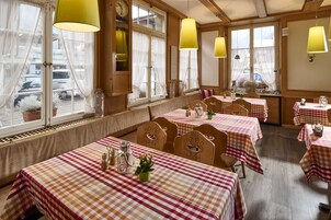 Un restaurante con manteles a cuadros, sillas de madera y lámparas colgantes amarillas.