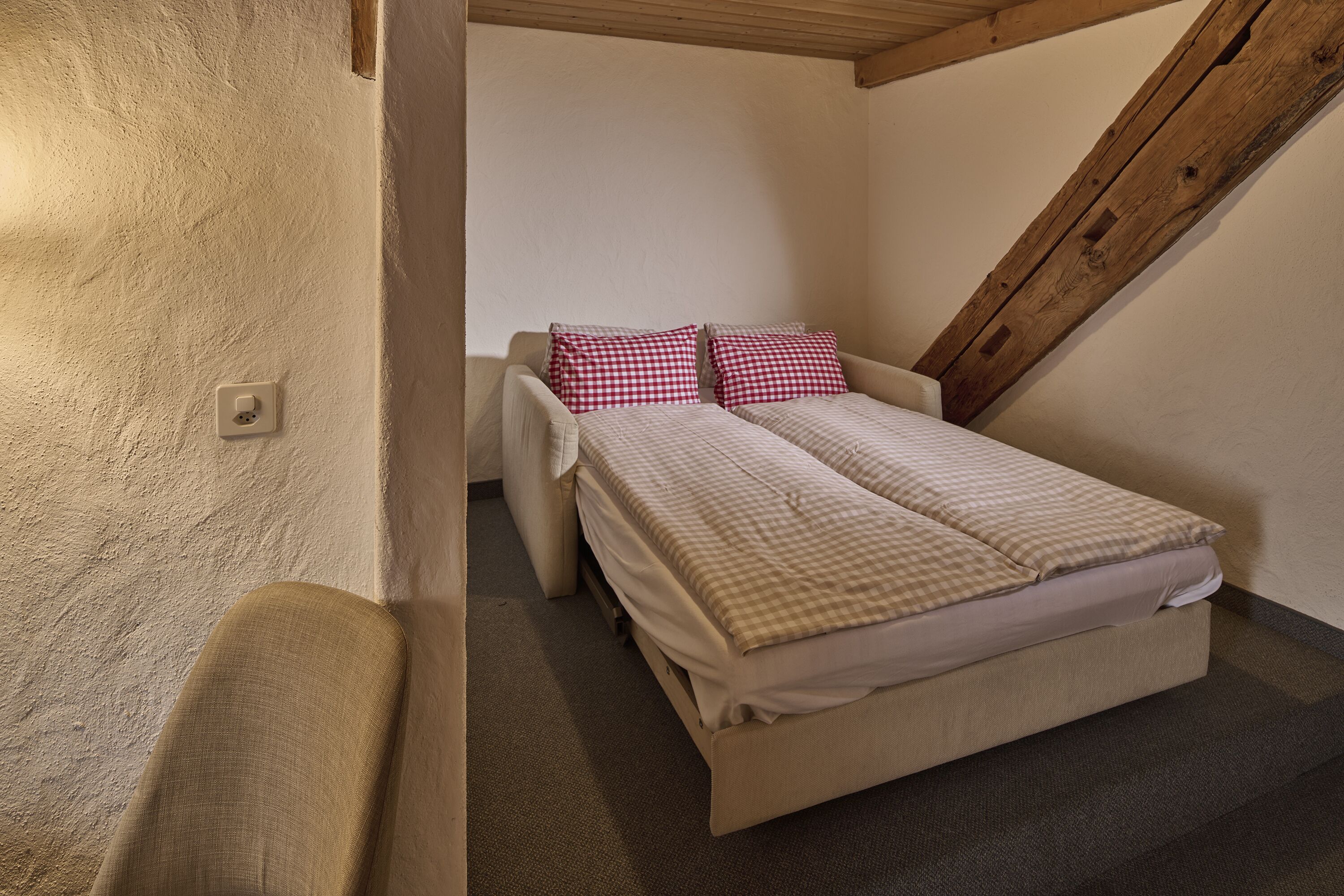 Una habitación pequeña y acogedora con una cama individual, una silla y una viga de techo de madera.
