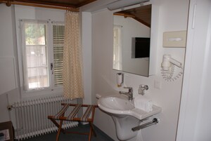Un baño con lavamanos blanco, un espejo, toallero, radiador y una ventana con persianas.