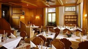 Un restaurante con interiores de madera, varias mesas dispuestas con manteles blancos, velas y detalles dorados.