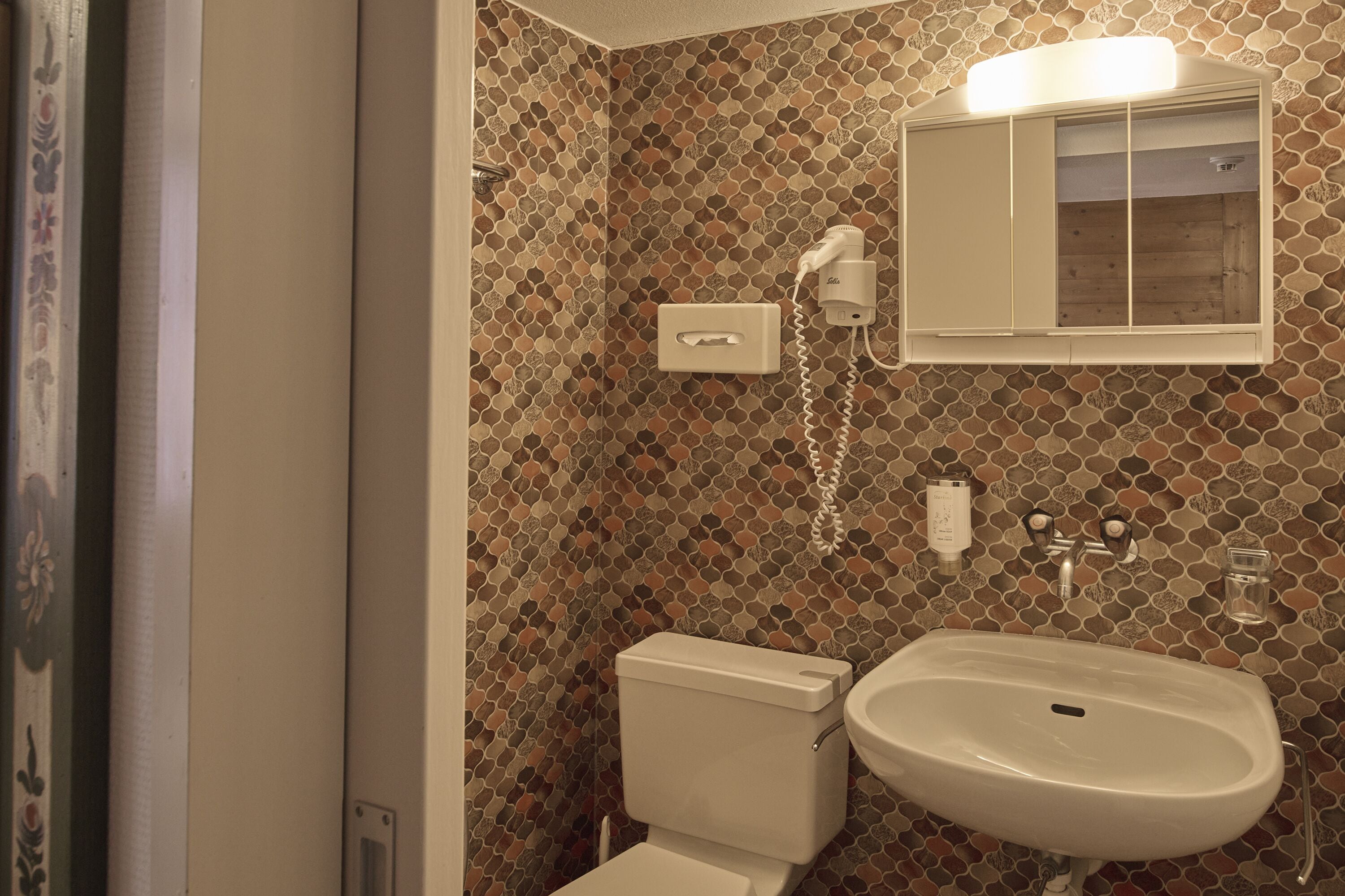 A bathroom with a mosaic tile wall, a toilet, a sink, and a mirror above the sink.