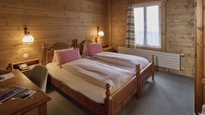 Una habitación con paneles de madera, dos camas, un escritorio y una ventana con cortinas.
