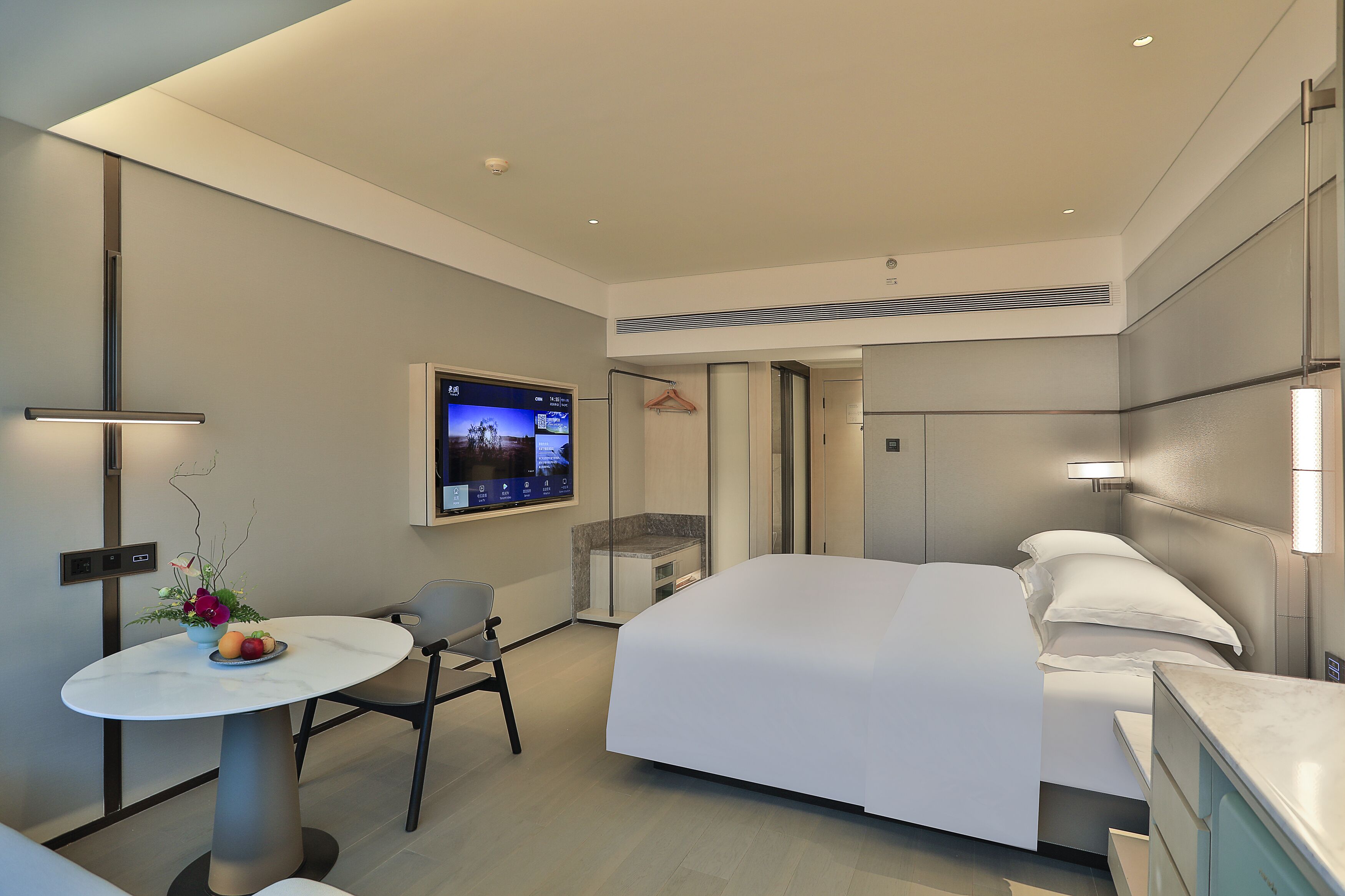 Une chambre d’hôtel moderne équipée d’un lit, d’un bureau avec une chaise, d’un téléviseur fixé au mur et d’un petit coin salon avec une table et des chaises.