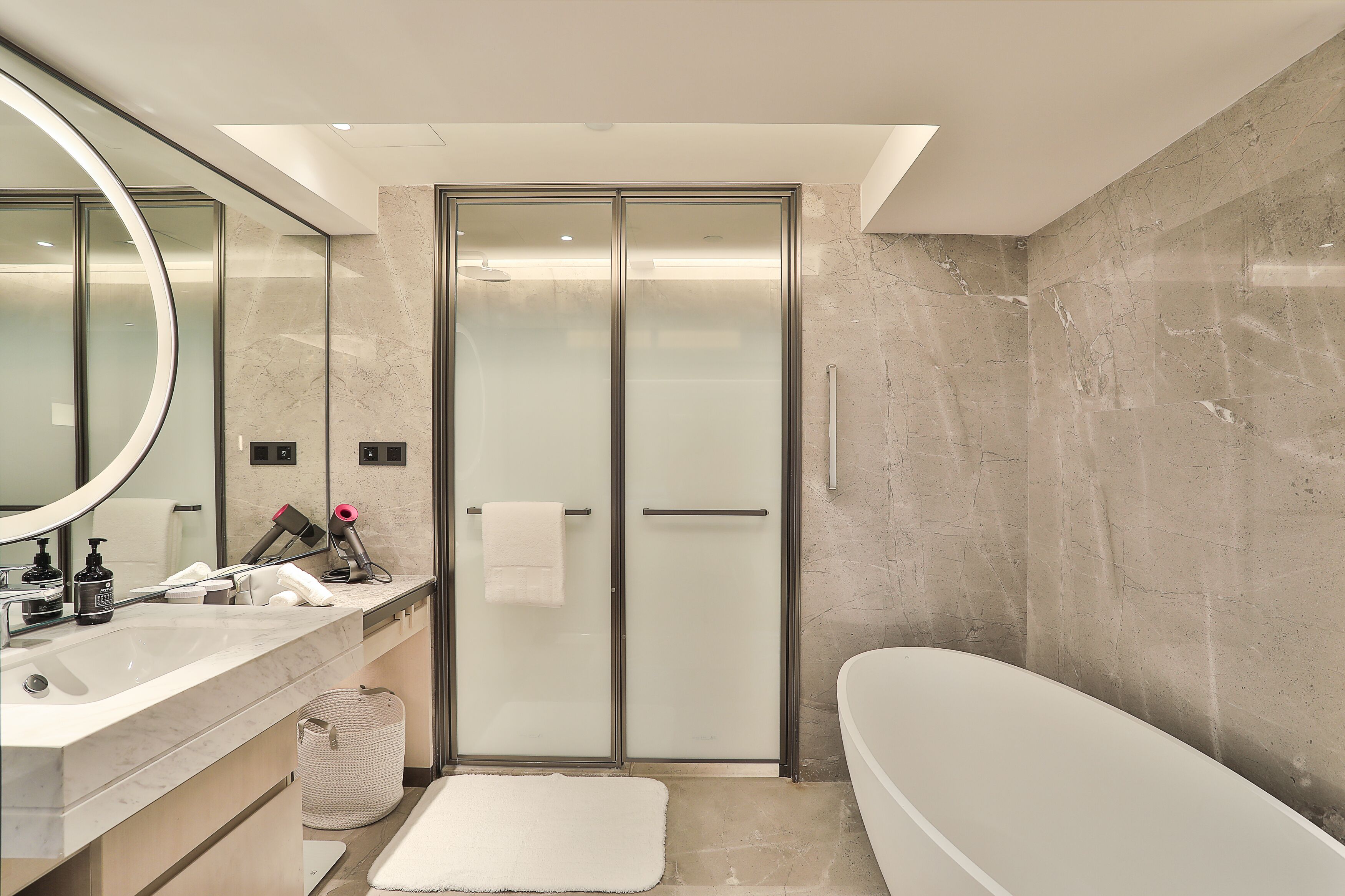 A modern bathroom with a large mirror, a white bathtub, and a glass-enclosed shower.