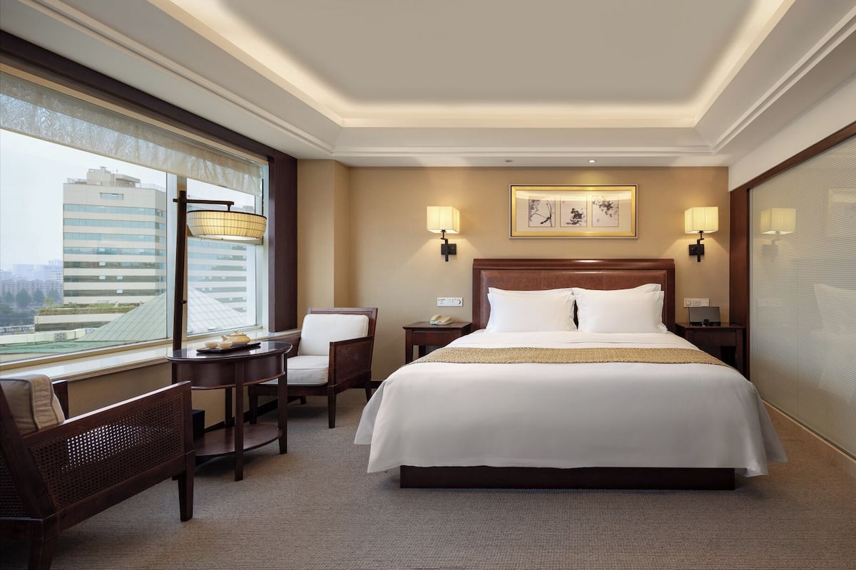A hotel room with a large bed, two bedside tables, a chair, a desk, and a window with a view of buildings.