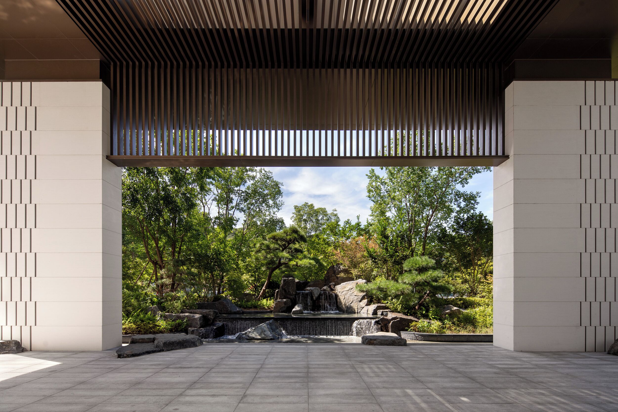 A modern architectural structure with a stone floor, a water feature, and a view of a natural landscape.