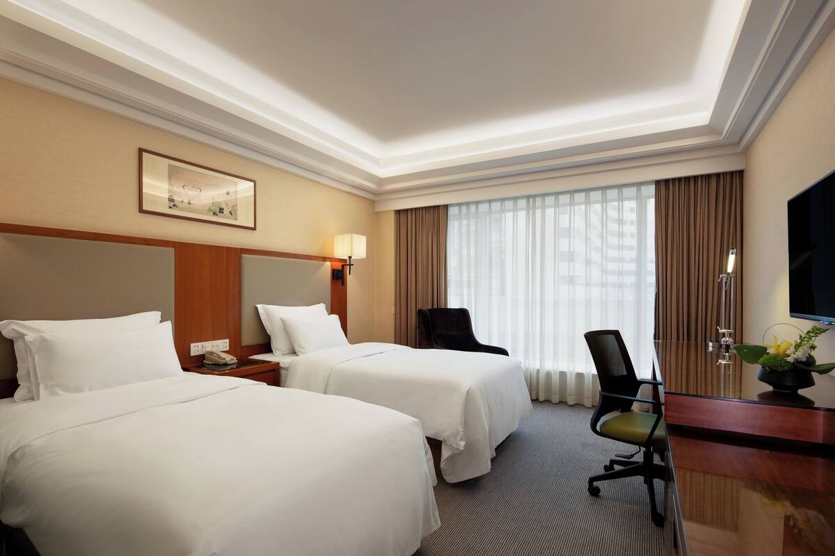 A hotel room with two beds, a desk, a chair, a television, and a window with curtains.