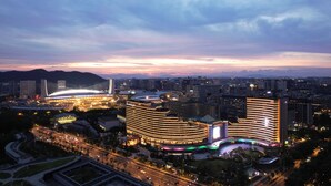 A modern hotel with a curved facade, surrounded by a well-lit urban area with a stadium in the background. - Zhejiang Narada Grand Hotel (Hangzhou)