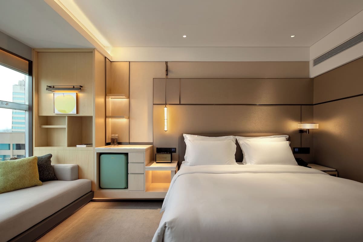 A modern hotel room with a large bed, bedside tables, a desk, and a sofa.