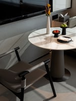 Un comedor moderno con una mesa redonda de mármol, dos sillas tapizadas, un florero con flores, un cuenco de fresas y un cuenco de manzanas verdes.