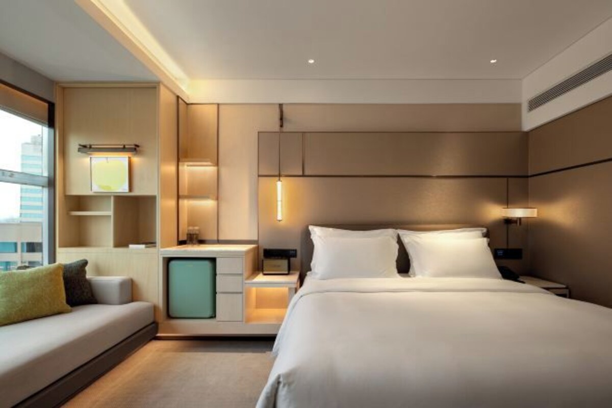 Una habitación de hotel moderna con una cama grande, un sofá, un escritorio con lámpara y vistas a la ciudad.