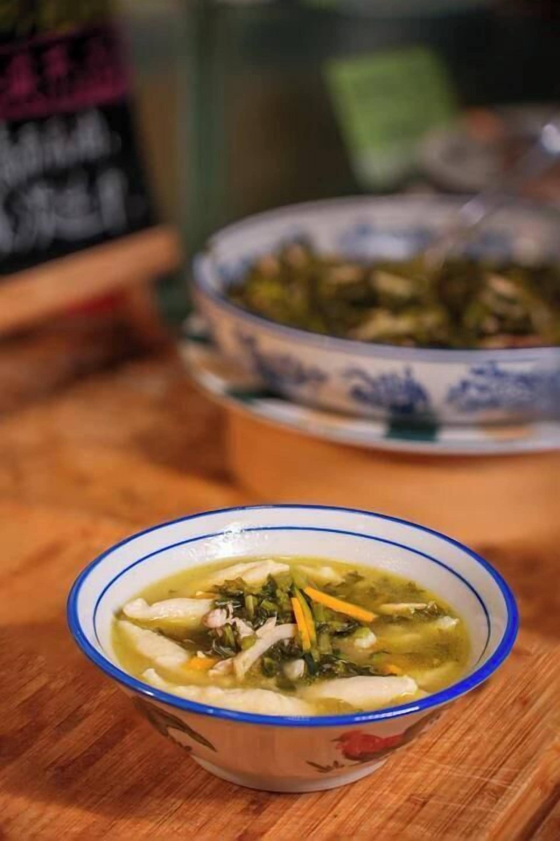 A bowl of soup with vegetables and meat, placed on a wooden surface.