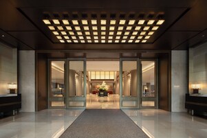 Un vestíbulo de hotel con puerta de vidrio de entrada, una recepción central y piso alfombrado.