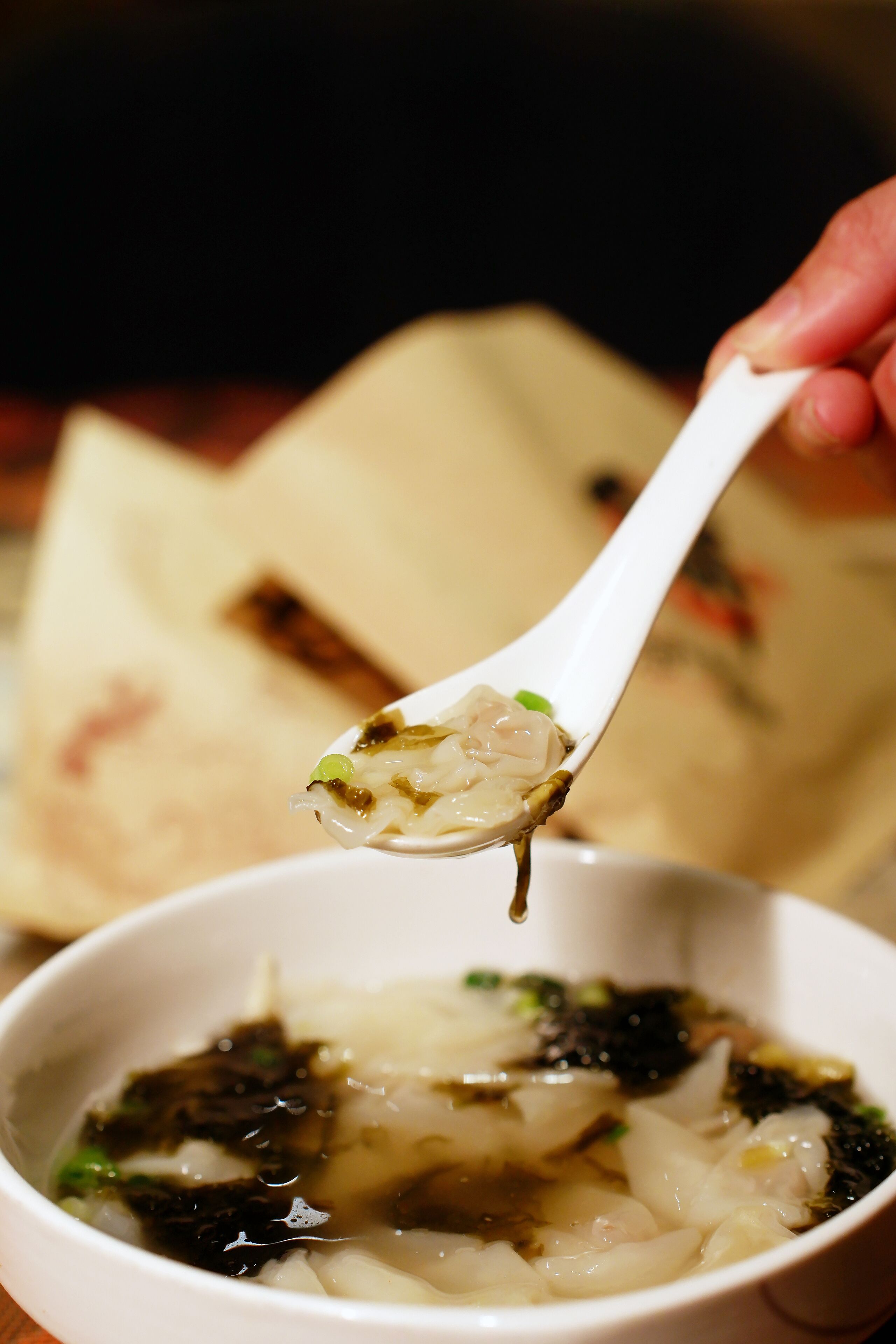 Un tazón de sopa con fideos y algas marinas, con una cuchara sirviendo parte del contenido.